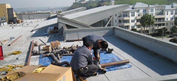 Two Splash Pluming plumbers repairing pipes on rooftop near coast